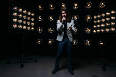 erkek şarkıcı parlak fenerler, çerçevede uzun saçlı sahne alanı üzerinde mikrofon ile sahne