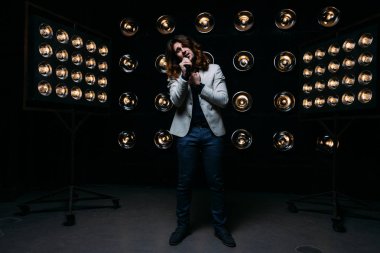 erkek şarkıcı parlak fenerler, çerçevede uzun saçlı sahne alanı üzerinde mikrofon ile sahne