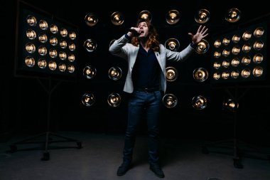 erkek şarkıcı parlak fenerler, çerçevede uzun saçlı sahne alanı üzerinde mikrofon ile sahne