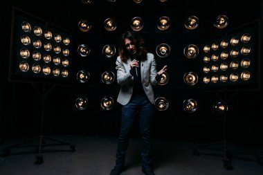 erkek şarkıcı parlak fenerler, çerçevede uzun saçlı sahne alanı üzerinde mikrofon ile sahne