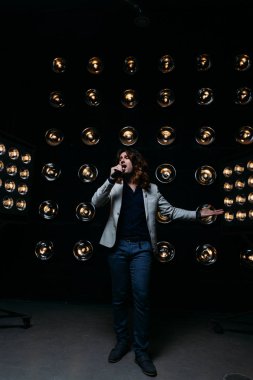 erkek şarkıcı parlak fenerler, çerçevede uzun saçlı sahne alanı üzerinde mikrofon ile sahne