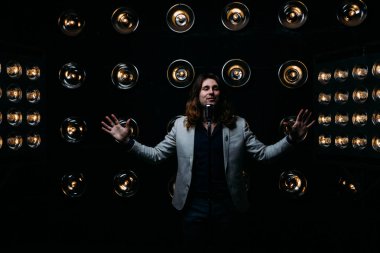 erkek şarkıcı parlak fenerler, çerçevede uzun saçlı sahne alanı üzerinde mikrofon ile sahne