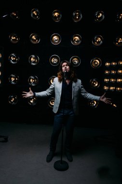 erkek şarkıcı parlak fenerler, çerçevede uzun saçlı sahne alanı üzerinde mikrofon ile sahne