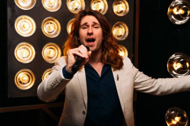 erkek şarkıcı parlak fenerler, çerçevede uzun saçlı sahne alanı üzerinde mikrofon ile sahne