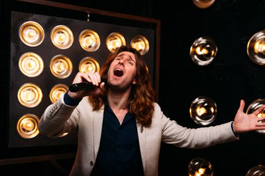 erkek şarkıcı parlak fenerler, çerçevede uzun saçlı sahne alanı üzerinde mikrofon ile sahne