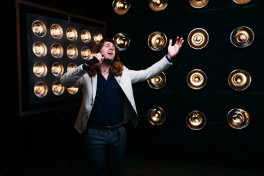 erkek şarkıcı parlak fenerler, çerçevede uzun saçlı sahne alanı üzerinde mikrofon ile sahne