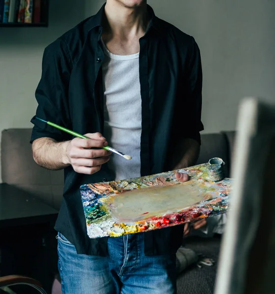 El artista sostiene una paleta con pinturas y un pincel y va a pintar sobre lienzo — Foto de Stock