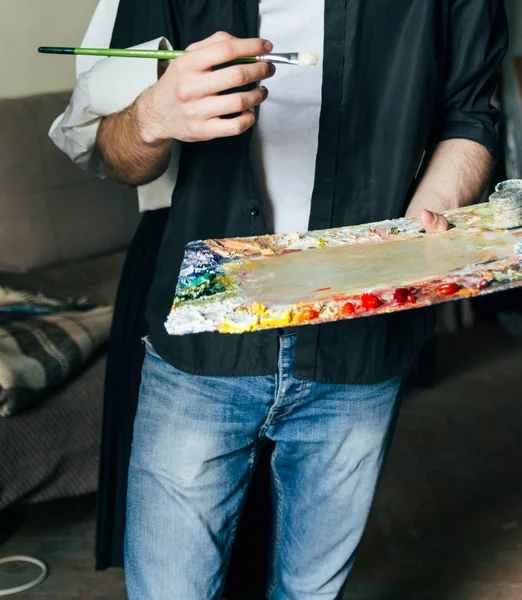 Un hombre sostiene en su mano una paleta con pinturas y un pincel, y detrás de él abrazan — Foto de Stock