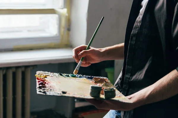 Frente a la ventana el artista sostiene una paleta con pinturas y un pincel y va a pintar sobre lienzo — Foto de Stock