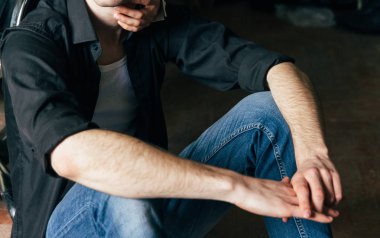 bir adam kollarını boynuna bir ahşap zemin üzerinde oturuyor. bir adam bir sandalye yanında oturuyor