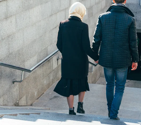 a couple walks, walks through the city, holding hands, arm, rear view. dressed in a black coat and a black jacket, the girl has a white scarf