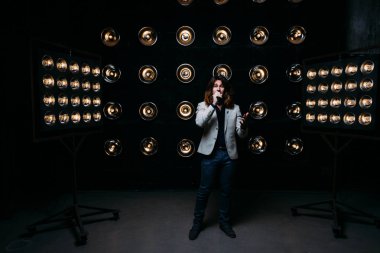 erkek şarkıcı parlak fenerler, çerçevede uzun saçlı sahne alanı üzerinde mikrofon ile sahne