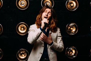 erkek şarkıcı parlak fenerler, çerçevede uzun saçlı sahne alanı üzerinde mikrofon ile sahne