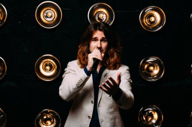 erkek şarkıcı parlak fenerler, çerçevede uzun saçlı sahne alanı üzerinde mikrofon ile sahne