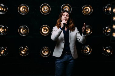 erkek şarkıcı parlak fenerler, çerçevede uzun saçlı sahne alanı üzerinde mikrofon ile sahne