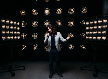 erkek şarkıcı parlak fenerler, çerçevede uzun saçlı sahne alanı üzerinde mikrofon ile sahne