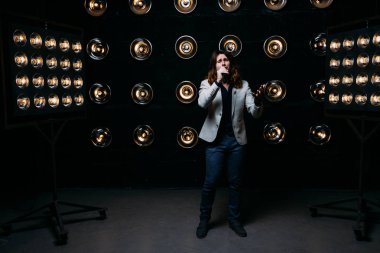 erkek şarkıcı parlak fenerler, çerçevede uzun saçlı sahne alanı üzerinde mikrofon ile sahne