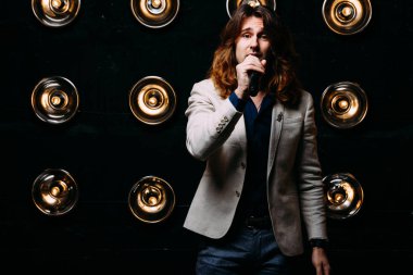 erkek şarkıcı parlak fenerler, çerçevede uzun saçlı sahne alanı üzerinde mikrofon ile sahne