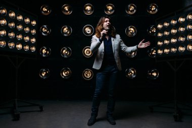 erkek şarkıcı parlak fenerler, çerçevede uzun saçlı sahne alanı üzerinde mikrofon ile sahne