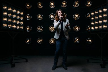 erkek şarkıcı parlak fenerler, çerçevede uzun saçlı sahne alanı üzerinde mikrofon ile sahne