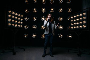 erkek şarkıcı parlak fenerler, çerçevede uzun saçlı sahne alanı üzerinde mikrofon ile sahne