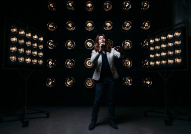 erkek şarkıcı parlak fenerler, çerçevede uzun saçlı sahne alanı üzerinde mikrofon ile sahne