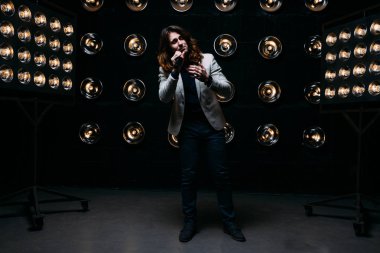 erkek şarkıcı parlak fenerler, çerçevede uzun saçlı sahne alanı üzerinde mikrofon ile sahne