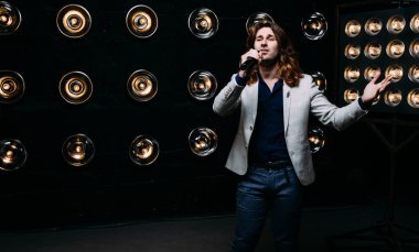 erkek şarkıcı parlak fenerler, çerçevede uzun saçlı sahne alanı üzerinde mikrofon ile sahne