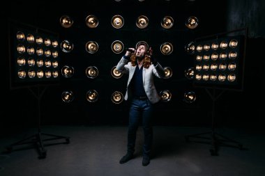 erkek şarkıcı parlak fenerler, çerçevede uzun saçlı sahne alanı üzerinde mikrofon ile sahne