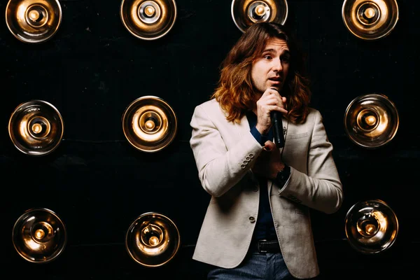 erkek şarkıcı parlak fenerler, çerçevede uzun saçlı sahne alanı üzerinde mikrofon ile sahne