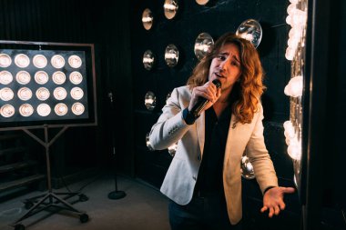 erkek şarkıcı parlak fenerler, çerçevede uzun saçlı sahne alanı üzerinde mikrofon ile sahne