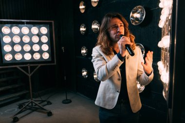 erkek şarkıcı parlak fenerler, çerçevede uzun saçlı sahne alanı üzerinde mikrofon ile sahne