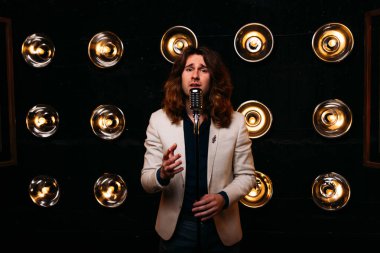 erkek şarkıcı parlak fenerler, çerçevede uzun saçlı sahne alanı üzerinde mikrofon ile sahne