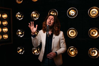 erkek şarkıcı parlak fenerler, çerçevede uzun saçlı sahne alanı üzerinde mikrofon ile sahne