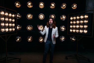 erkek şarkıcı parlak fenerler, çerçevede uzun saçlı sahne alanı üzerinde mikrofon ile sahne