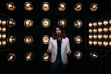 erkek şarkıcı parlak fenerler, çerçevede uzun saçlı sahne alanı üzerinde mikrofon ile sahne