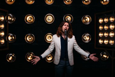 erkek şarkıcı parlak fenerler, çerçevede uzun saçlı sahne alanı üzerinde mikrofon ile sahne