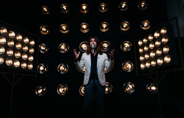 erkek şarkıcı parlak fenerler, çerçevede uzun saçlı sahne alanı üzerinde mikrofon ile sahne