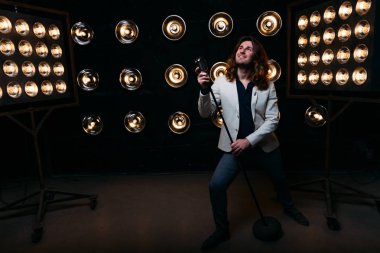 erkek şarkıcı parlak fenerler, çerçevede uzun saçlı sahne alanı üzerinde mikrofon ile sahne