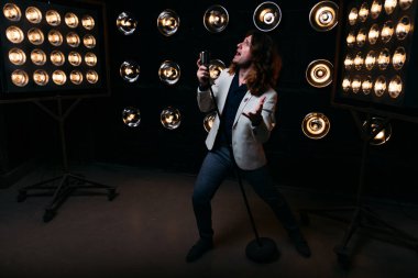 erkek şarkıcı parlak fenerler, çerçevede uzun saçlı sahne alanı üzerinde mikrofon ile sahne