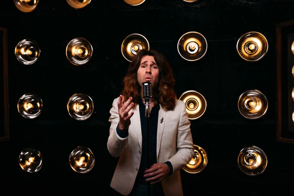erkek şarkıcı parlak fenerler, çerçevede uzun saçlı sahne alanı üzerinde mikrofon ile sahne
