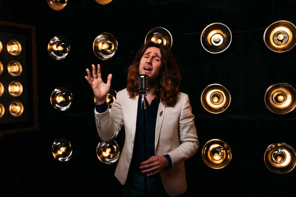 erkek şarkıcı parlak fenerler, çerçevede uzun saçlı sahne alanı üzerinde mikrofon ile sahne