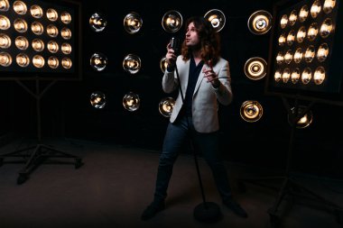 erkek şarkıcı parlak fenerler, çerçevede uzun saçlı sahne alanı üzerinde mikrofon ile sahne