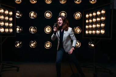 erkek şarkıcı parlak fenerler, çerçevede uzun saçlı sahne alanı üzerinde mikrofon ile sahne