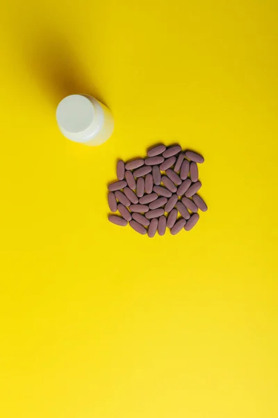 Bílý box pro tablety stojí na žlutém pozadí vedle lži práškama podlouhlé, fialová. — Stock fotografie