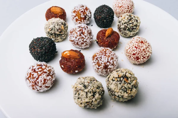 sweets from dried fruits with nuts and sesame seeds Tasty energy balls with dried fruits and nuts in coconut chips on a white plate