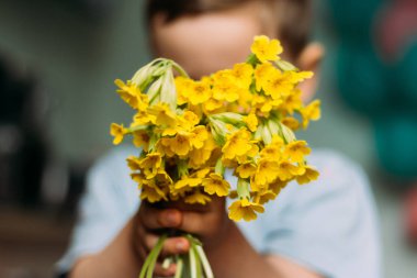 Çocuk bulanık bir buket sarı çiçek arkasında saklandığını tereddüt. Annem için bir hediye. bir buket vermek. hediye - bulanık buket çiçek. yaz