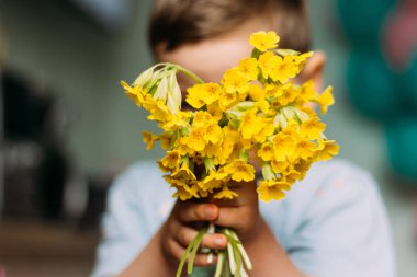 Çocuk bulanık bir buket sarı çiçek arkasında saklandığını tereddüt. Annem için bir hediye. bir buket vermek. hediye - bulanık buket çiçek. yaz