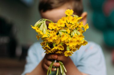 Çocuk bulanık bir buket sarı çiçek arkasında saklandığını tereddüt. Annem için bir hediye. bir buket vermek. hediye - bulanık buket çiçek. yaz