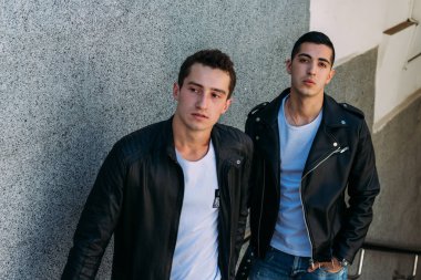 beklenti seksi poz korkuluk yakınındaki mans. çekici bir genç adamın bir siyah deri ceket, beyaz bir T-shirt ve beyaz spor ayakkabı korkuluk yakın duruyor. dostluk. iki model. Giysi gösterilen